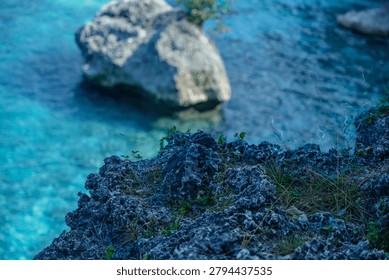  Close up of sharp volcanic rock texture on the coast with blurry crystal clear blue ocean water in the background.