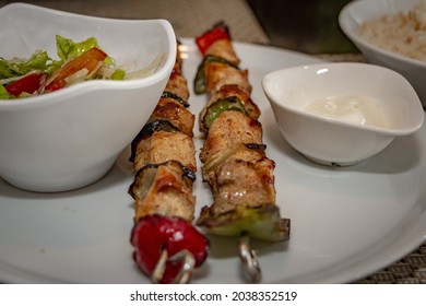 A Close Up Of Shish Taouk And White Sesame Paste And Salad On A White Plate