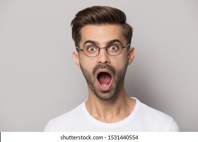 Close up of shocked caucasian young man in glasses isolated on grey studio background look at camera feel stunned, amazed male in spectacles surprised by good promotion, great unexpected news