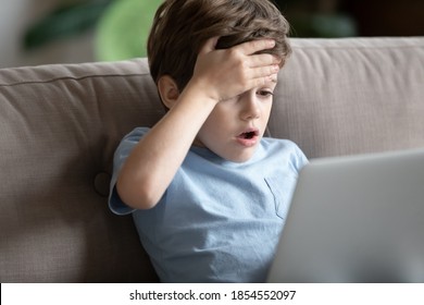 Close Up Shocked Little Boy With Open Mouth Looking At Laptop Screen, Using Computer Alone, Touching Forehead, Unhappy Amazed Kid Child Having Problem With Device, Sitting On Couch At Home