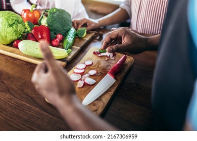 Close Up Shoot Of Black Man Holding Sharp Knife Cutting Vegetables On Wooden Board, Making Fresh Salad Using Organic Ingredients.