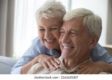 Close Up Shot Affectionate Smiling Middle Aged Wife Embrace Husband Pensioner From Behind Massage Shoulders Of Beloved Man Express Love Care Devotion. Romantic Cheerful Old Age Couple Hug Touch Heads