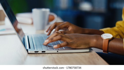 Close up shot of African American female hands typing on laptop while sitting at office desk indoors. Woman fingers tapping and texting on computer keyboard while working in cabinet. Work concept