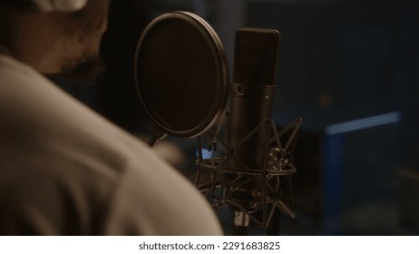 Close up shot of African American singer dancing and singing lyrical composition into microphone in soundproof room. Professional vocalist works in sound recording studio. Concept of music production.