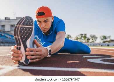 Close up shot of athlete runner young male stretching his leg on race track in stadium, preparing for working out. Caucasian man exercising outdoors wearing blue sportswear. Sport, people, lifestyle - Powered by Shutterstock