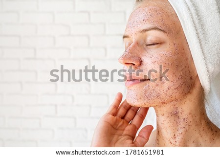 Close up shot of attractive smiling woman applying scrub on her face skin. Facial cleansing concept. Spa and beauty. Natural cosmetics