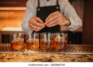 A close up shot of a bartender in a green apron making Old Fashioned cocktails in a restaurant. Focus on glasses and hands. Concept of hospitality and bartending. Horizontal image.