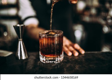 A Close Up Shot Of A Bartender Pouring Whiskey. Classic Old Fashioned Cocktail Served With A Cube Of Ice. Concept Of Bourbon Whisky, Spirits And Alcohol.