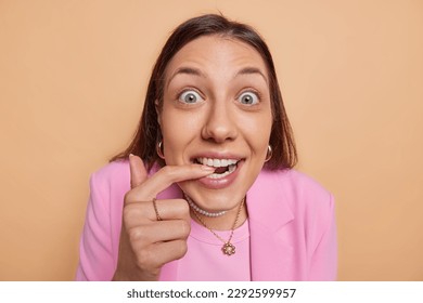 Close up shot of beautiful dark haired woman bites finger and stares at camera with bugged eyes cannot believes in something impressive has surprised curious expression wears formal pink jacket - Shutterstock ID 2292599957