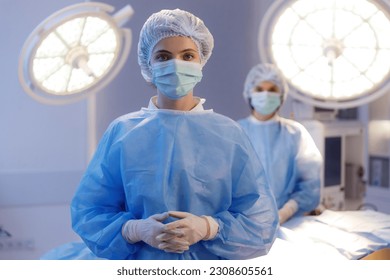 A close up shot of a beautiful nurse wearing scrubs, a medical mask and a medical hairnet standing in a hospital room and behind her another nurse - Powered by Shutterstock