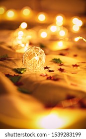 Close up shot of blurred golden Christmas lights with tiny stars and Christmas tree decorations, on rumpled bed sheets, making cozy and festive atmosphere. Festive bukeh background with lights.