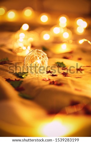 Close up shot of blurred golden Christmas lights with tiny stars and Christmas tree decorations, on rumpled bed sheets, making cozy and festive atmosphere. Festive bukeh background with lights.
