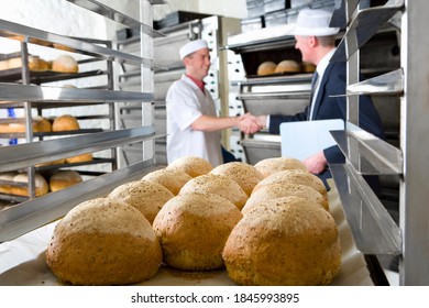 A close up shot of bread loaves with an inspector shaking hands with a baker in a blur background. - Powered by Shutterstock