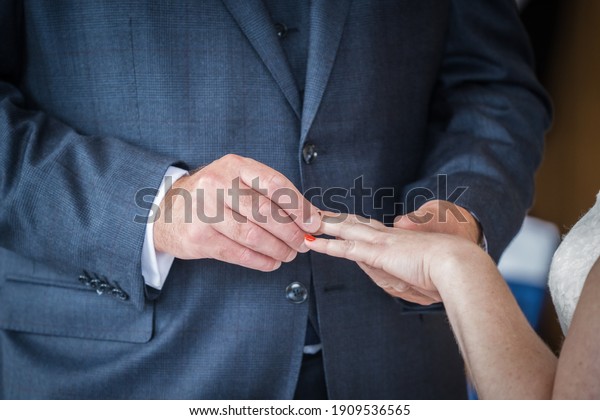 Close up shot of bride holding out hand as groom\
at wedding ceremony placing ring on finger whilst saying vows and I\
do to seal the marriage