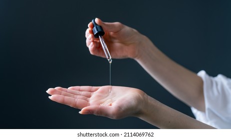 Close Up Shot Of A Caucasian Hand Holding An Eye Dropper While Dropping Some Serum Into Her Palm Isolated On A Grey Background. Beauty Skincare.