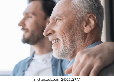 Close up shot of a caucasian young adult son supporting his old elderly senior man looking at the window in future together at home. Happy father`s day! I love you, dad! - Powered by Shutterstock