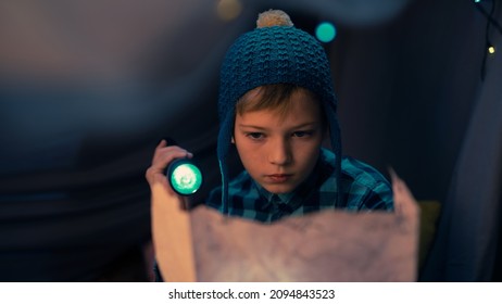 Close Up Shot of a Caucasian Young Boy Holding the Treasure Map and a Flashlight, Looking Serious As He Tries to Decipher the Code, Sitting and Hiding in a Dark Tent During The Night.