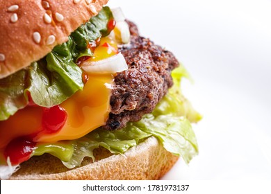 Close Up Shot Of A Classic Burger With A Beef Patty, Melt Away
 Cheese, Onions, Ketchup, Tomato Slices And Salad Leaves In A Burger Bun With Sesame On A White Plate