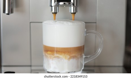 Close Up Shot Of Coffee Pouring Into Glass Cup With Milk, Making Cappuccino Using The Automatic Coffee Machine. Beverage Drink For Breakfast.