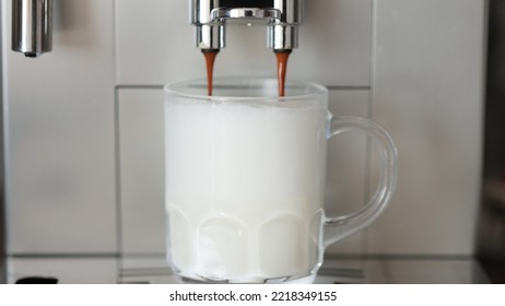 Close Up Shot Of Coffee Pouring Into Glass Cup With Milk, Making Cappuccino Using The Automatic Coffee Machine. Beverage Drink For Breakfast.