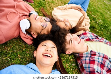 Close up shot of confident multiracial group of students smiling lying in a circle on the grass. Cheerful and happy young people having fun together. Diversity people spending leisure time.