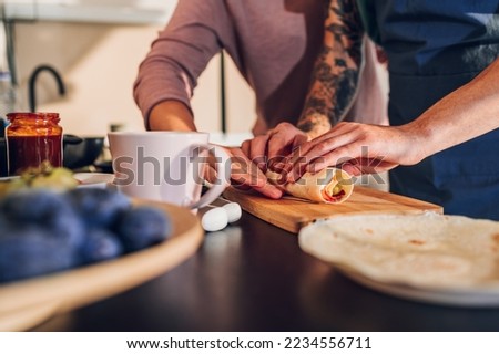 Close shot of a couple hands while cooking together and making breakfast in the kitchen. Focus on a hands rolling a burrito.Enjoying morning time together. Copy space.