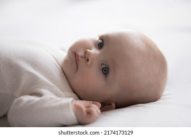 Close up shot cute newborn baby in bodysuit lying down alone on bed. Adorable infant rests on white bedsheets, staring at camera looking peaceful. Infancy, healthcare and paediatrics, babyhood concept - Shutterstock ID 2174173129