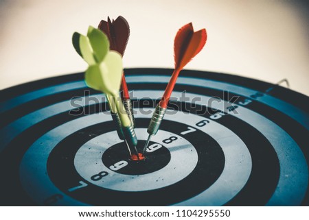 Close up shot of the dart arrow hit on bulleyes of dartboard to represent that the business reached the target of company with dark tone picture style. Target and goal as concept.