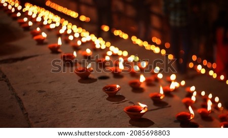 Close up shot of Dev Deepawali 2021 festival, Earthen lamps lit on the stairs leading to the Ganges with selective focus. 
Thousands of diyas (oil lamps) are lined up on the stairs near Ganges.