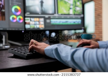 Close up shot of digital video editor sitting at multi monitor workstation desk while working on movie footage. Creative post production house videographer improving film frames visual quality.