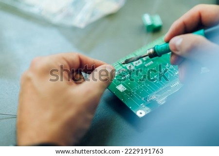 Close shot of a electronics engineer hands working in a professional workshop with tin soldering parts. Repairing electronic devices and working with electric equipment. Fixing circular board.