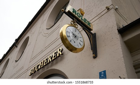 Close up shot the facade of a high end jewelry and watch shop with huge pocket watch Rolex hanging sign and Bucherer brand sign.  Munich, Germany.  August 2019.                              