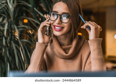 Close up shot of female business professional talking on smartphone while sitting at coffee shop. Happy positive lady in glasses sitting cafeteria have mobile conversation, discussion work plan