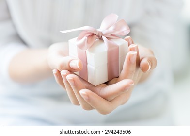 Close up shot of female hands holding a small gift wrapped with pink ribbon. Small gift in the hands of a woman indoor. Shallow depth of field with focus on the little box. - Shutterstock ID 294243506