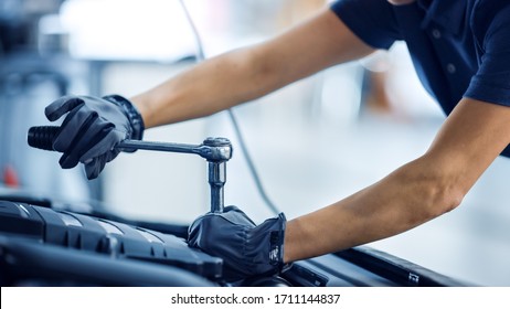 Close Up Shot Of A Female Mechanic Working On A Vehicle In A Car Service. Empowering Woman Fixing The Engine. She's Using A Ratchet. Modern Clean Workshop.