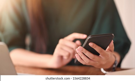 Close up shot female using her smartphone on wood table. - Powered by Shutterstock