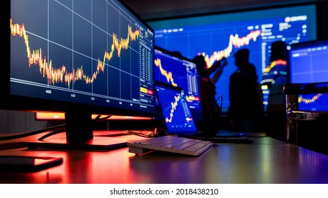 Close Up Shot Of Financial Analysis Graph Chart Stock Exchange Bitcoin Cryptocurrency Report On Computer Screen Monitors And Laptop On Working In Trading Room While Broker Meeting In Shadow Behind.