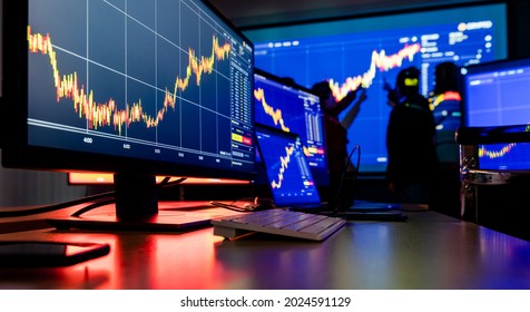 Close Up Shot Of Financial Analysis Graph Chart Stock Exchange Bitcoin Cryptocurrency Report On Computer Screen Monitors And Laptop On Working In Trading Room While Broker Meeting In Shadow Behind.