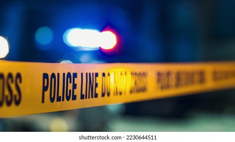 Close Up Shot Focused on Yellow Tape Showing Text "Police Line Do Not Cross". Restricted Area of a Crime Scene. Bokeh Background with Flickering Siren Lights. Forensics Team Working on a Case - Shutterstock ID 2230644511
