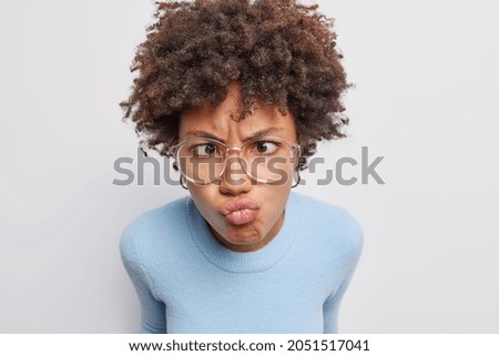 Close up shot of funny Afro American woman makes grimace crosses eyes and pouts lips at camera wears transparent glasses casual turtleneck isolated over white background. Face expressions concept