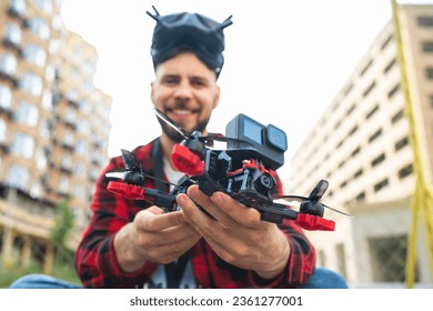Close up shot of generic design fpv multicopter drone in hands of smiling young casually dressed professional pilot man making settings before starting operating experience. Focus on hands with copter