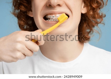 Close up shot of a ginger haired teen boy with braces, thoroughly cleaning his teeth, isolated on a blue background. Dental care practice concept