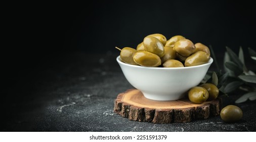 Close up shot of green olives in a white bowl on the wooden stand with olive leaves on a black background. Traditional Greek and Italian food. - Powered by Shutterstock