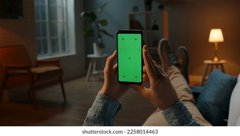 Close up shot of guy lying on couch at night, holding a smartphone with chroma key mock up green screen - technology, connections, communications concept  - Powered by Shutterstock