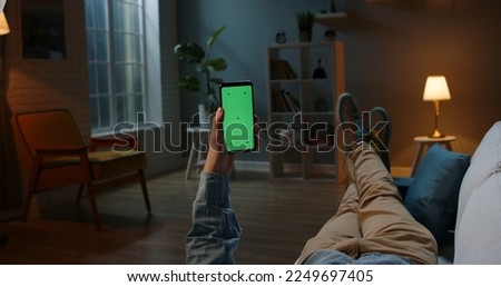 Close up shot of guy lying on couch at night, holding a smartphone with chroma key mock up green screen - technology, connections, communications concept 