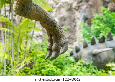 Close Up Shot From A Hand, Claw Of Dinosaur (theropod) On Green Jungle With Stegosaurus Background.