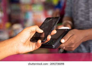 Close Up Shot Of Hand Paying Money By Taping Mobile Phone To Swiping Machine At Retail Kirana Or Groceries Store - Concept Of Contectless And One Tap Digital Payment