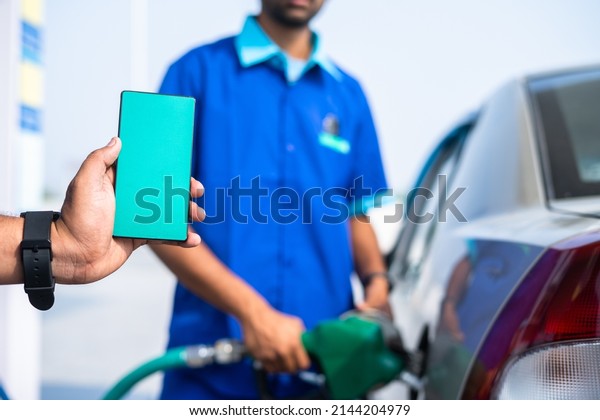close up shot of hand showing green\
screen mobile phone while worker filling petrol on car - concept of\
application advertisement, promotion and\
offers.