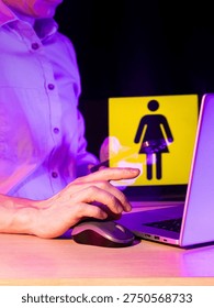Close shot of hand using mouse, laptop displaying scissors trimming female gender symbol in violet light.