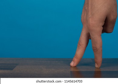 Close up shot of a hand, walking the two fingers on wooden table on blue background.